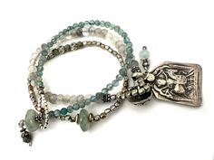 Handmade Boho Bracelets featuring a Vintage Hindu Durga Warrior Goddess Silver Charm (about 1 1/2" x 7/8") pairs with small faceted Gray and Cloudy Quartz beads.  There is a 925 Sterling Silver Embossed Button that serves as the clasp, added to the set is a small Aqua glass beaded bracelet with an Aventurine Bead clasp.  Last is small silver tone beads with coordinating Aqua colored beads.  The set is charming, unique and perfect for the Warrior Woman in us all. Specifics ✥ Small Green Bracele 7.5"   ✥ Gray Quartz Bracelet 7.75" ✥ Silver Stretch Bracelet 6.25" Inner Diameter ✥ Includes Gift Packaging In a world of mass production, Kálon Style specializes in meticulously designed, exquisite jewelry and home decor you can be assured are as rare and beautiful as you!  There is a large variety Aqua Gemstone, Gray Quartz, Statement Bracelets, Warrior Goddess, Glass Beaded Bracelet, Bracelets Boho, Artisan Bracelets, Aqua Glass, Bracelets Silver