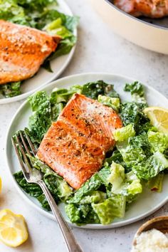 two plates with salmon, lettuce and lemon wedges