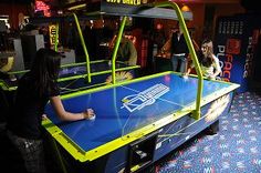 two people playing video games in a room with blue carpet and neon signs on the walls