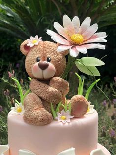 a teddy bear sitting on top of a pink cake with daisies in the foreground