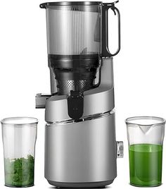 a juicer with two glasses next to it on a white surface and one is filled with green liquid