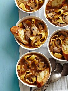 four white bowls filled with soup on top of a blue table next to silver spoons