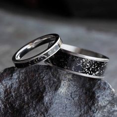 two wedding bands with black and white speckles are sitting on top of a rock