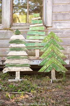 three wooden christmas trees sitting in front of a window on the ground next to grass