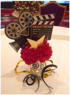 a movie themed centerpiece with red flowers and film claps on the top, sitting on a white table cloth