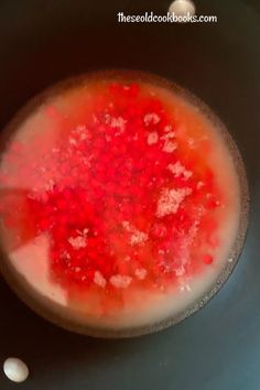 red liquid in a black bowl with white dots on the bottom and an orange substance to the side