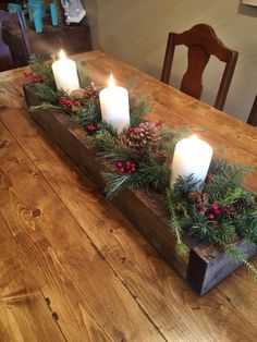 a wooden table topped with candles and greenery next to a candle holder filled with pine cones