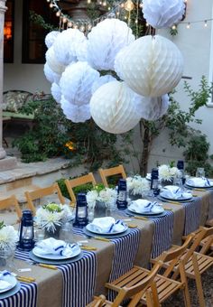 a table set up with blue and white place settings, paper lanterns and hanging decorations