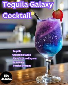 a purple and blue drink sitting on top of a wooden table next to a strawberry