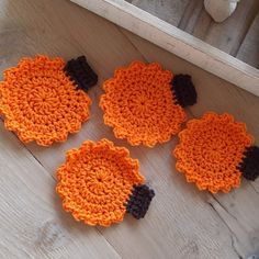 four crocheted pumpkin coasters sitting on top of a wooden floor next to a stuffed animal