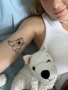 a woman with a small tattoo on her arm next to a white teddy bear in bed