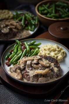 a white plate topped with meat covered in mushroom gravy next to green beans and mashed potatoes