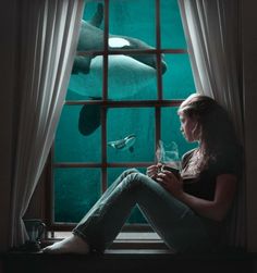 a woman sitting on a window sill looking out at an orca whale swimming in the ocean