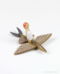 a paper doll sitting on top of an origami bird with a flower in its beak