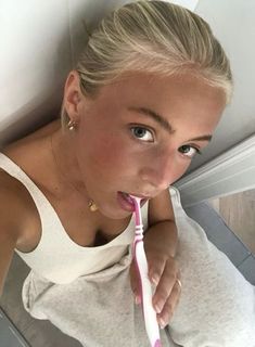 a woman brushing her teeth with a pink toothbrush