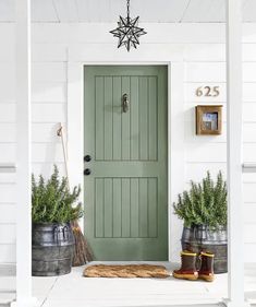 a green door and two buckets with plants on the front porch next to it