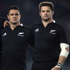 two rugby players standing next to each other in black uniforms with white gloves on their hands