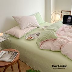 an unmade bed with pink and green comforters, pillows and a laptop on it