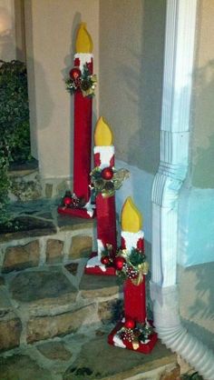 three red candles with christmas decorations on them are sitting in front of a stone wall