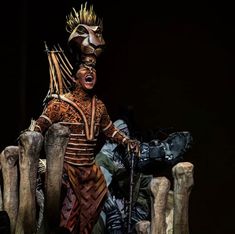 an elaborately dressed man sitting on a wooden bench in front of a black background