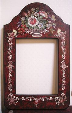 an ornate wooden frame with flowers and birds on the border is sitting on a shelf