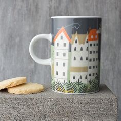 a coffee cup and some cookies on a concrete block with a gray background that has houses painted on it