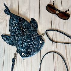 a blue fish purse sitting on top of a wooden floor next to sunglasses and eyeglasses