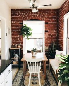 a room with a brick wall, white chairs and a rug on the floor in front of a window