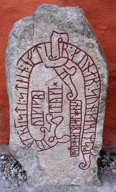 a rock with writing on it next to a red wall and some plants in the background