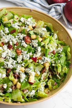 a salad in a wooden bowl with blue cheese and other toppings on the side