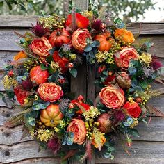 a wreath with orange flowers and greenery hanging on a wooden fence post in front of a tree