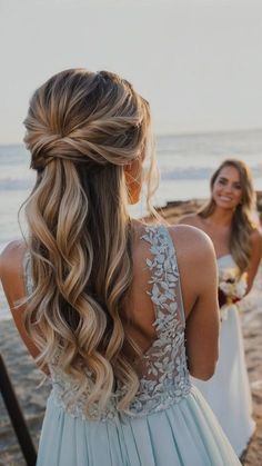 two women standing on the beach with their hair in half - up braids and one wearing