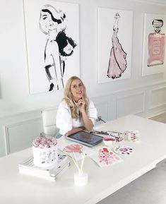 a woman sitting at a white table in front of paintings