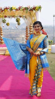 a woman dressed in yellow and blue walking down a pink carpeted aisle with flowers on it