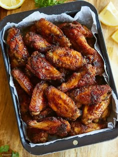 chicken wings are in a pan with lemon wedges and parsley on the side