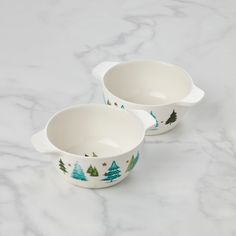 two white bowls with trees painted on them sitting on a marble countertop next to each other