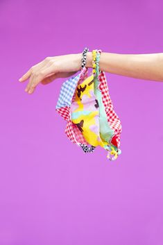 a person's hand is holding several colorful pieces of cloth in front of a purple background