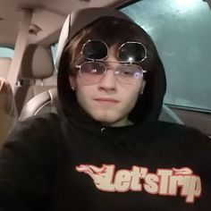 a young man wearing glasses and a hoodie sitting in a car looking at the camera