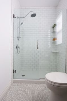 a white toilet sitting next to a shower in a bathroom on top of a tiled floor