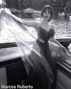 a woman in a long dress standing on the back of a boat wearing a veil