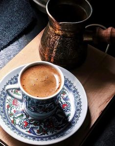 a cup of coffee sitting on top of a saucer next to a metal pitcher