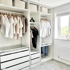 a white closet with clothes hanging on the shelves and drawers in front of a window