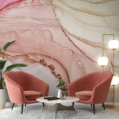 two pink chairs sitting next to each other in front of a large painting on the wall