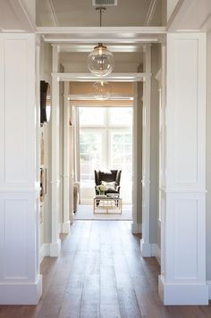 an empty hallway leading to a living room with a chair on the far side and a light fixture hanging from the ceiling