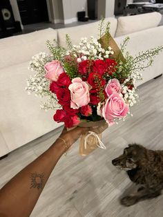 a person holding a bouquet of roses in their hand next to a dog on the floor