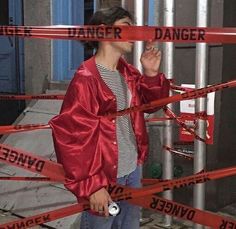 a young man standing in front of a fence with caution tape around him and covering his mouth