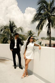 a man and woman standing next to each other on a roof with palm trees in the background