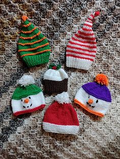 knitted hats with snowmen and christmas trees on them sitting on a couch in front of a blanket