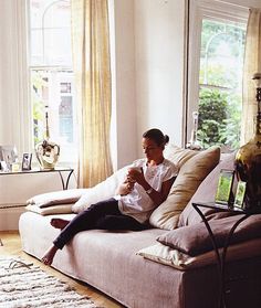 a woman sitting on top of a couch in front of a window holding a cup