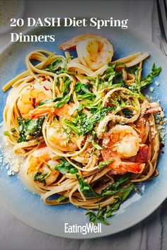 a blue plate topped with pasta and shrimp on top of a white table next to utensils